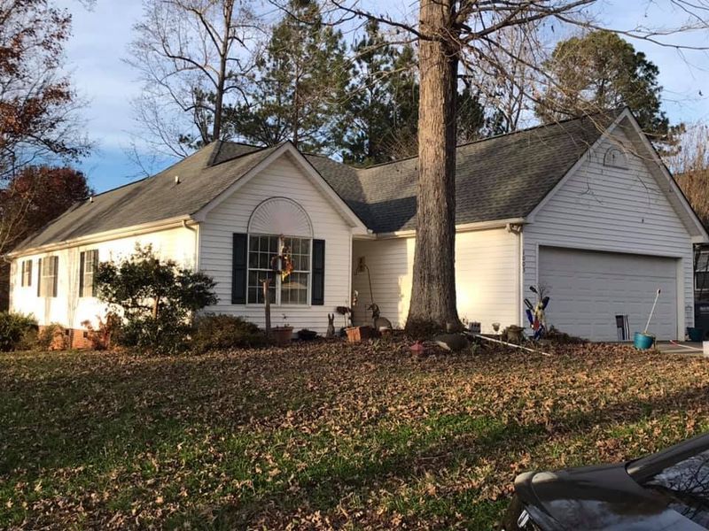 A white house with a garage and a tree in front of it