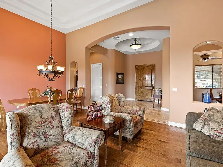 Elegant living room with peach walls, floral sofas, hardwood floors, and arched doorway into dining area