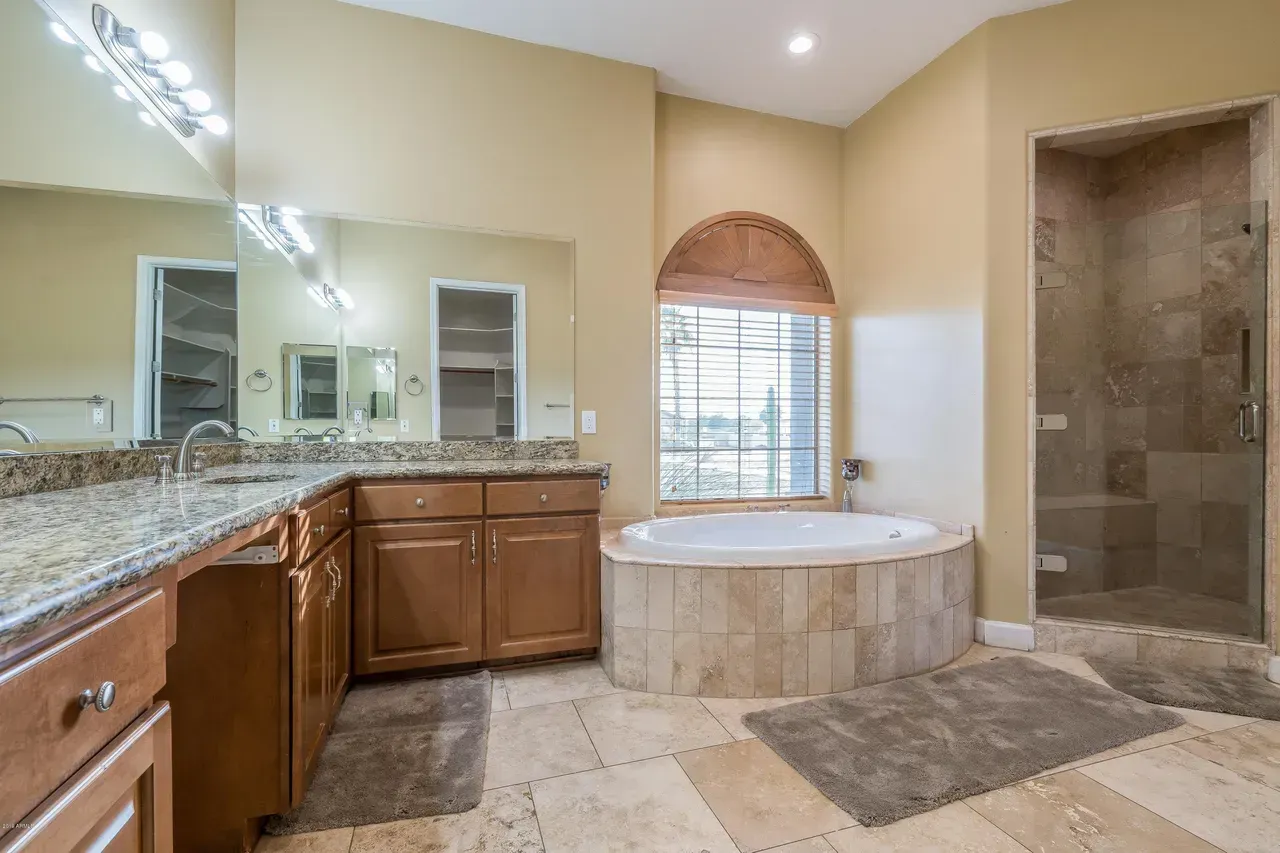 Spacious beige bathroom with double vanity, large mirror, soaking tub, and tiled walk-in shower