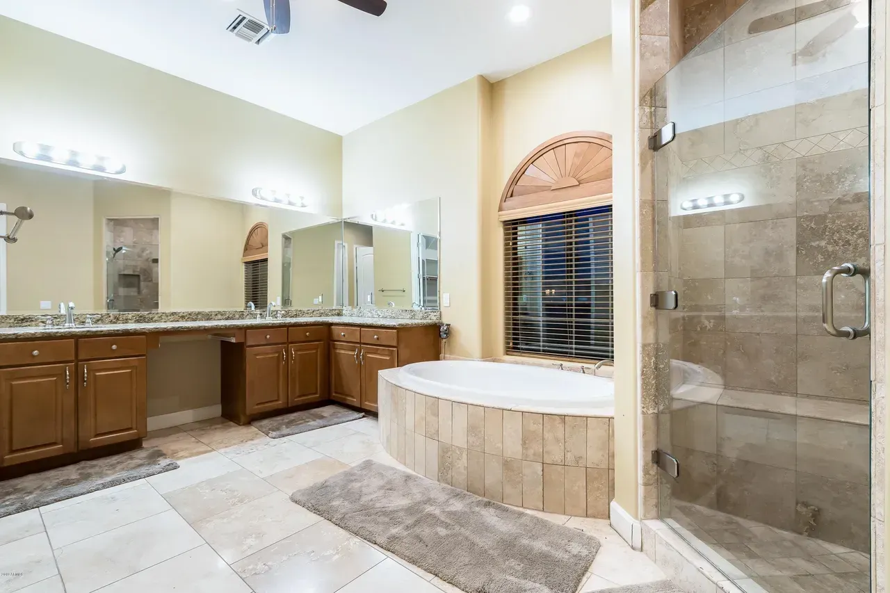 Spacious beige bathroom with double vanity, large mirrors, soaking tub, and glass shower enclosure