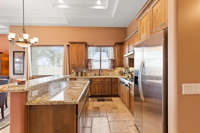 Spacious kitchen with granite island, wooden cabinets, stainless fridge, and tiled floor