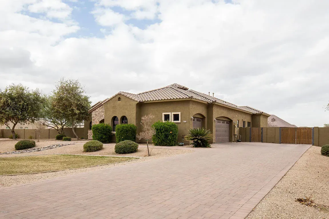 Suburban stucco house with a tiled roof and driveway under a cloudy sky