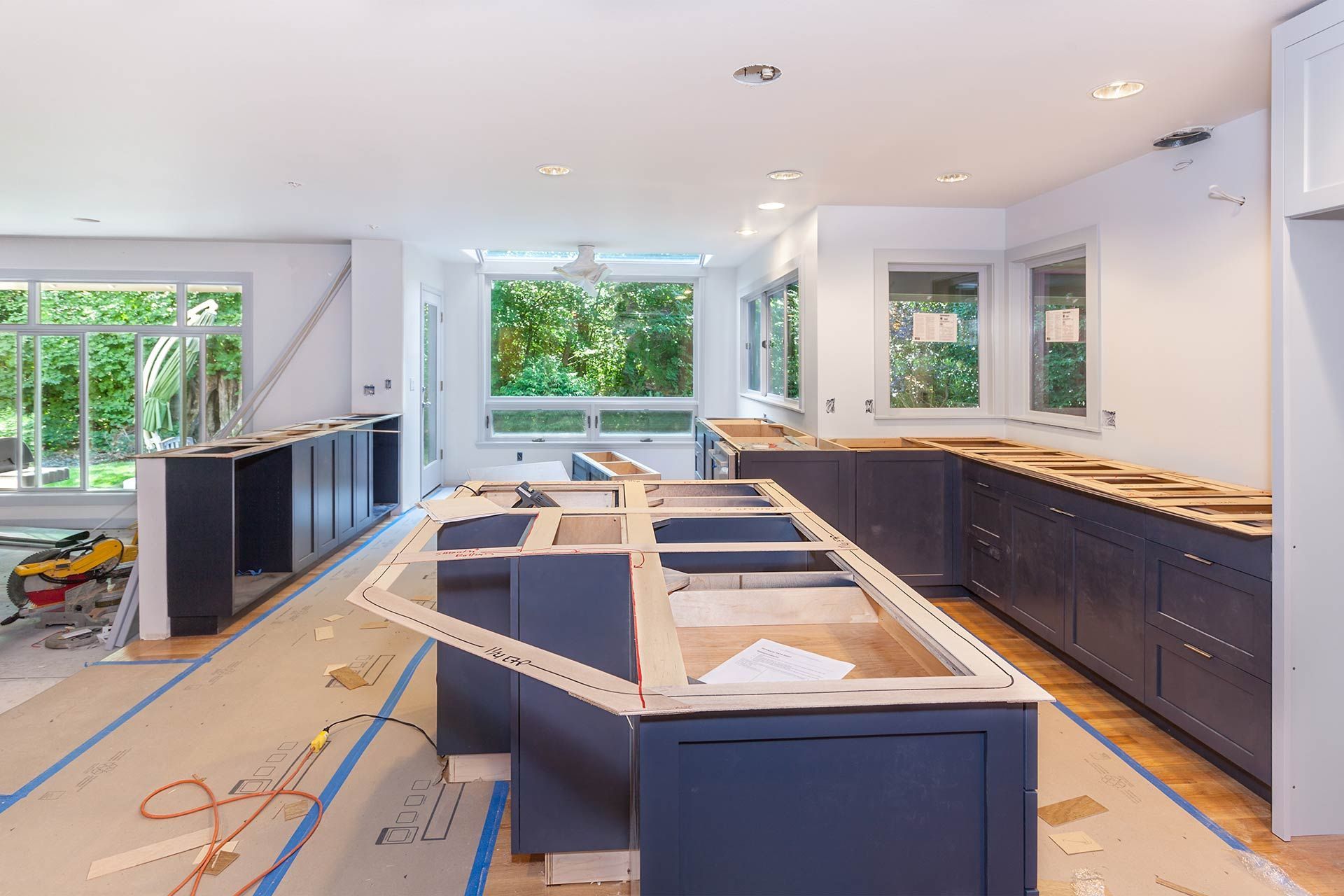 Partially renovated kitchen with dark cabinets, unfinished island, and daylight from large windows