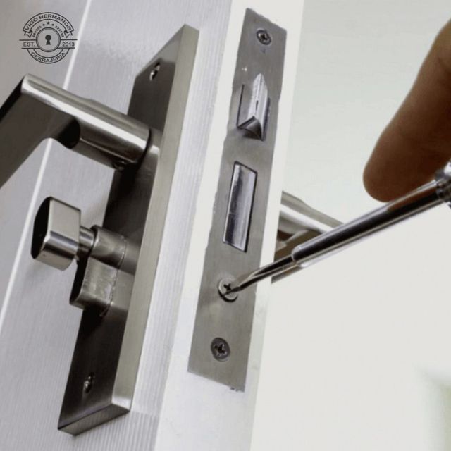 Persona usando un destornillador para ajustar una manija y cerradura de puerta plateada moderna en una puerta blanca.