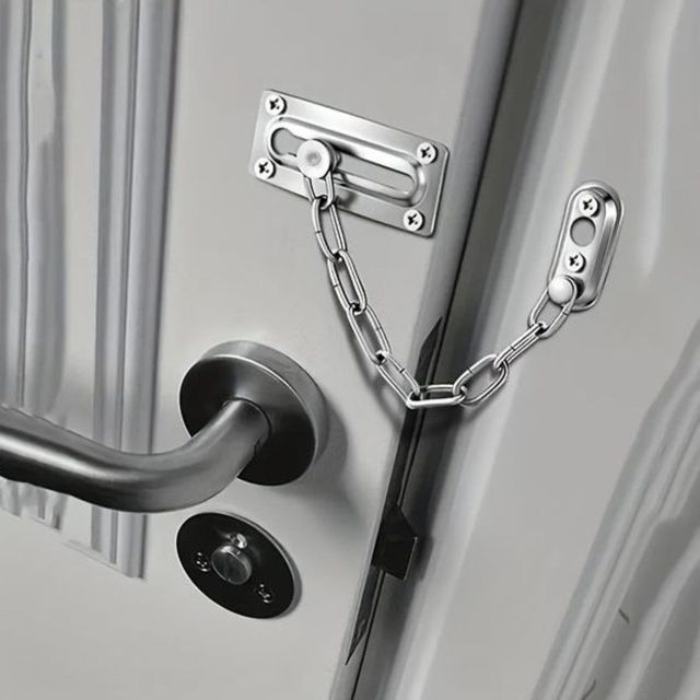 Cerradura de cadena plateada en una puerta gris con manija y cerrojo negros.