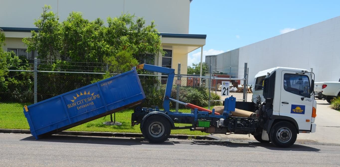 A Dump Truck With A Blue Dumpster Attached To It Is Parked In Front Of A Building — Sun City Skips In Bohle, QLD