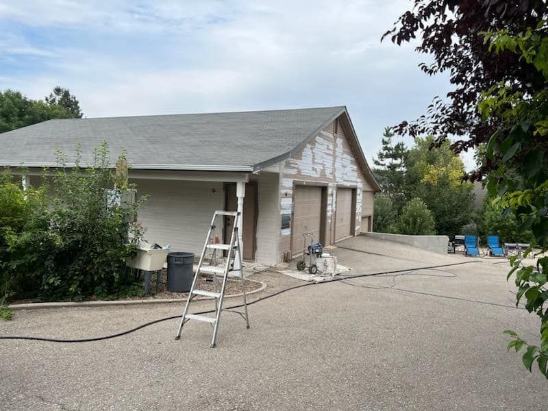 A large white house with a black roof is being painted.