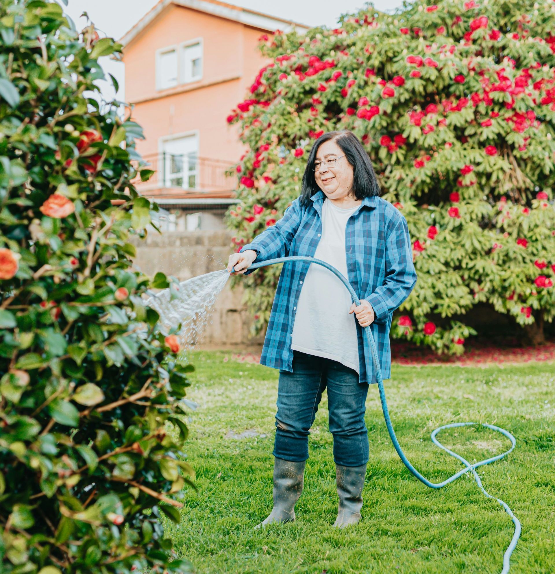 A woman is watering a bush with a hose.