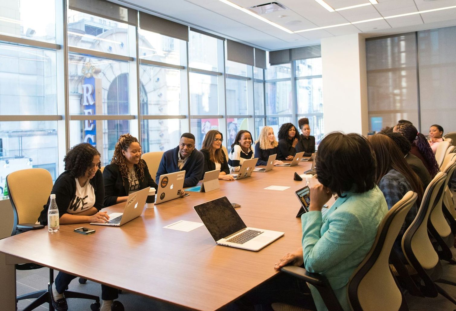 A group of people are sitting around a conference table with laptops.