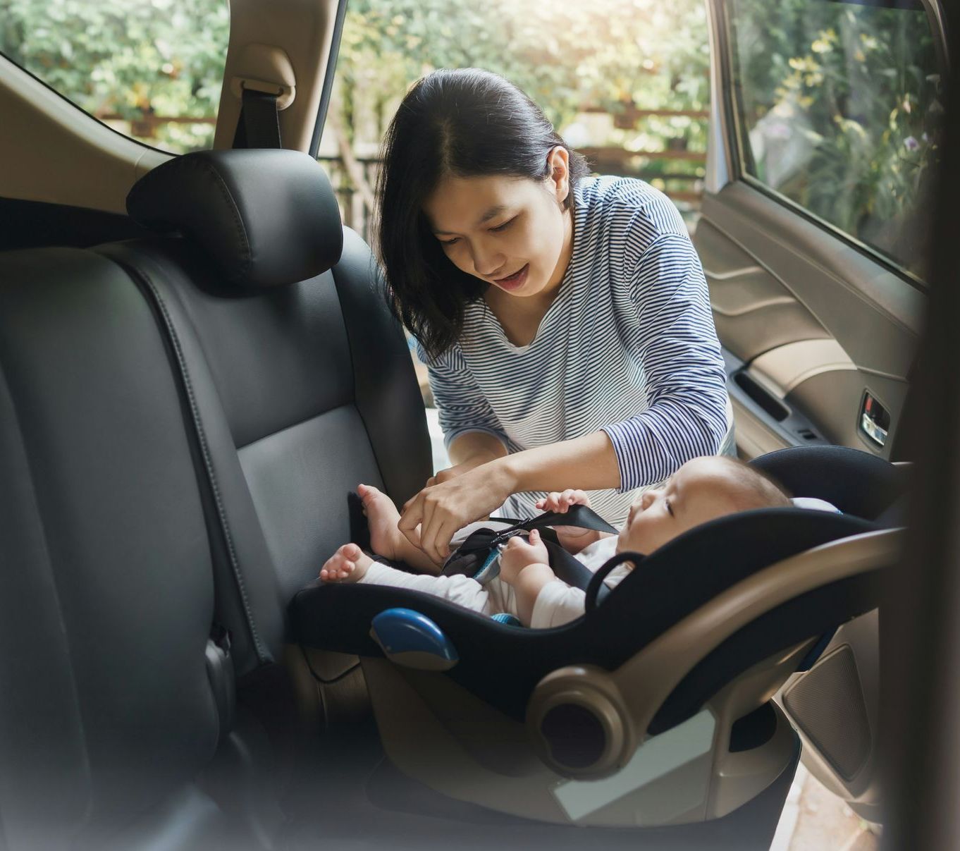 A woman is putting a baby in a car seat.