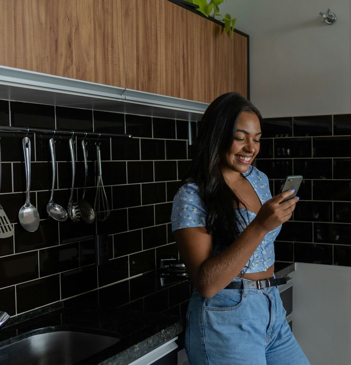 A woman is standing in a kitchen looking at her phone.