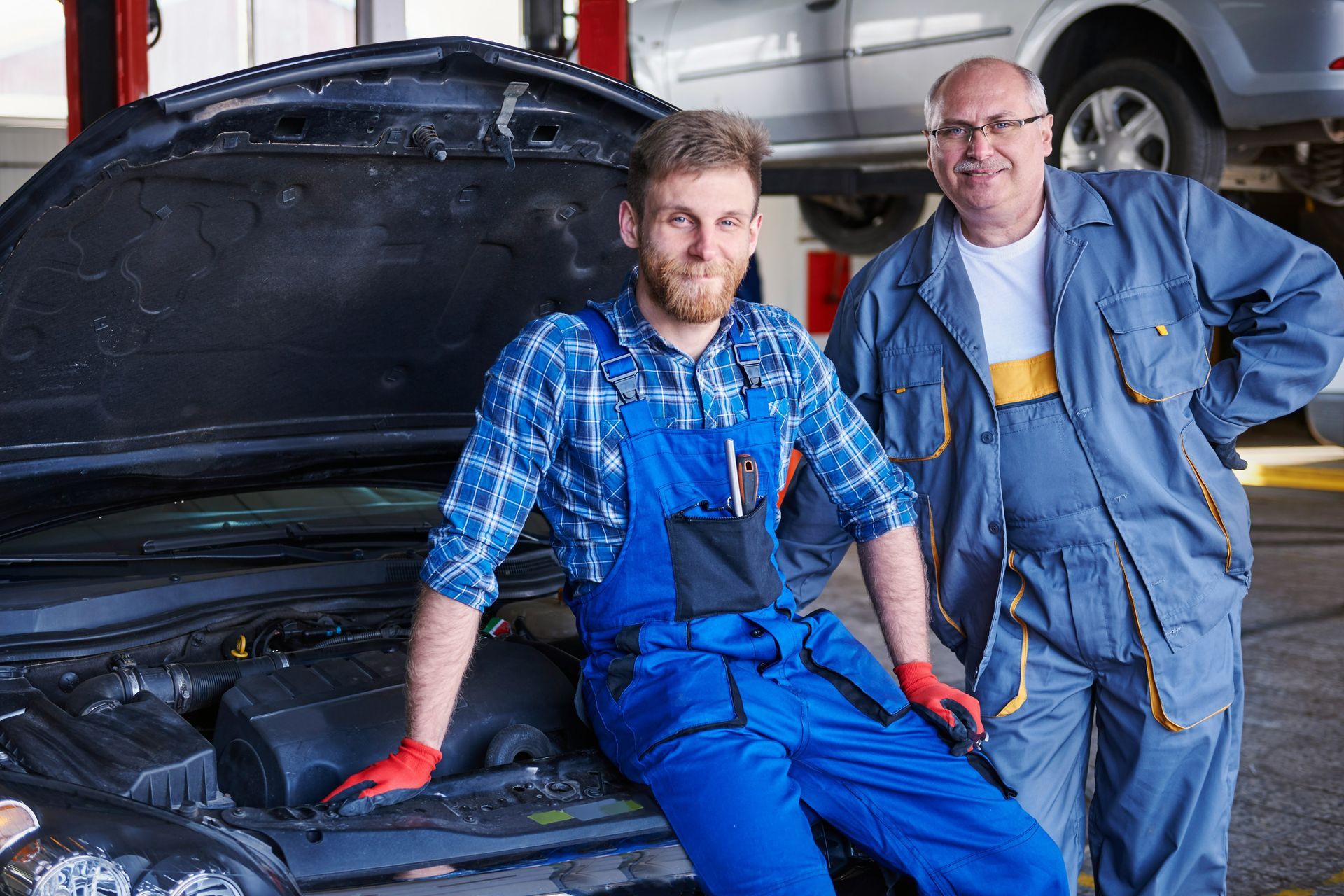 Two mechanics are standing next to each other in front of a car in a garage.