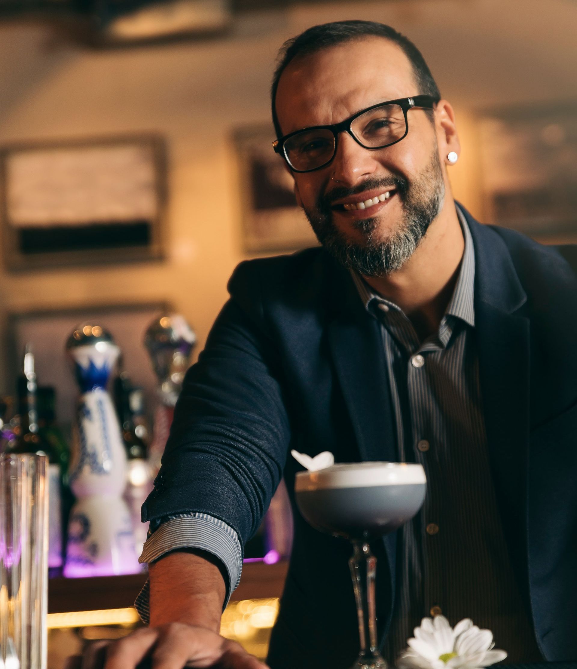 A man with glasses and a beard is behind a bar