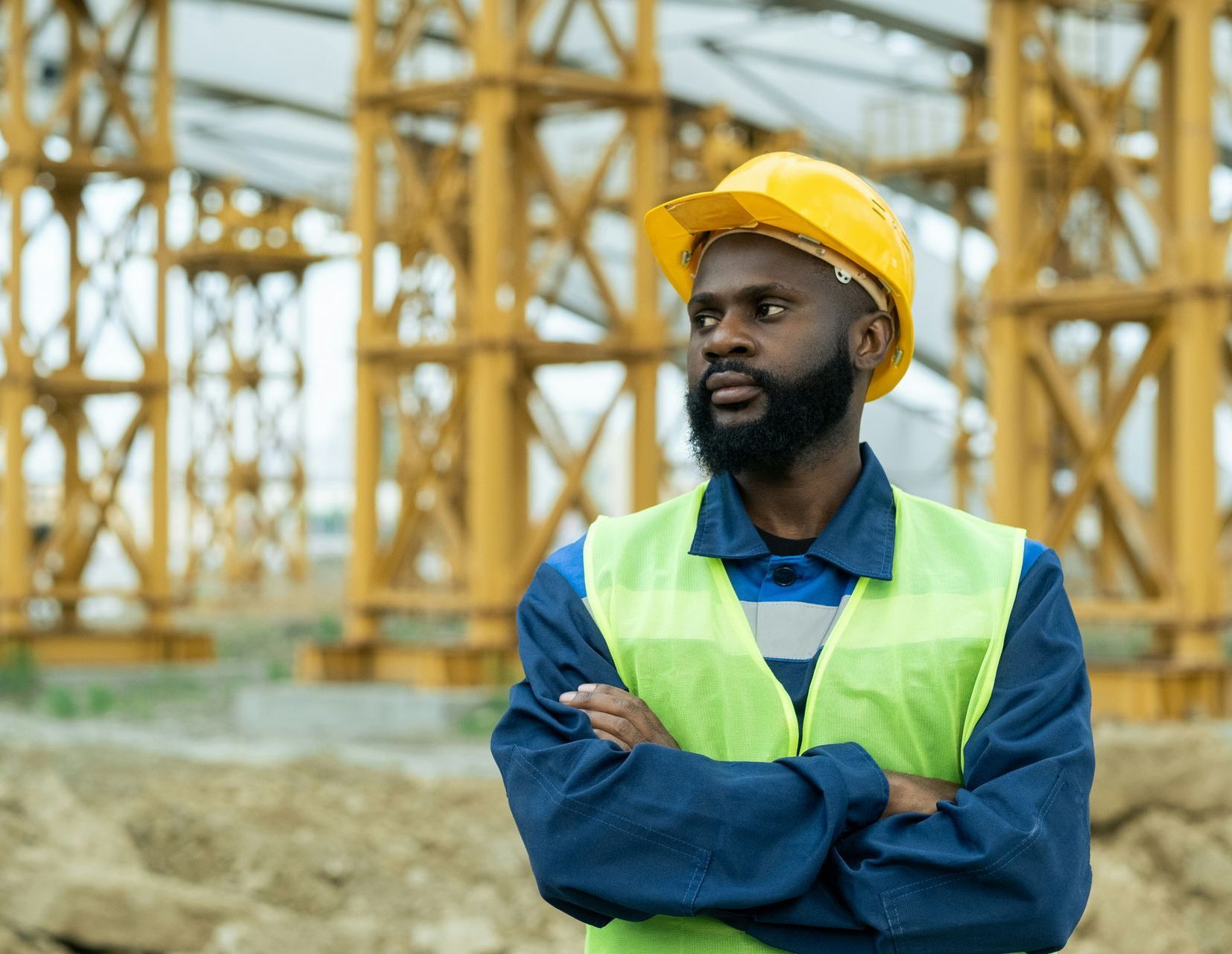 A man wearing a hard hat and safety vest is standing in front of a construction site.