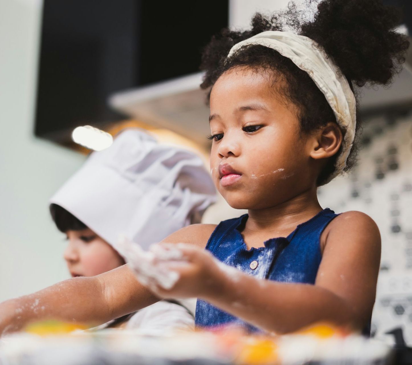 A little girl wearing a chef 's hat is cooking in a kitchen.