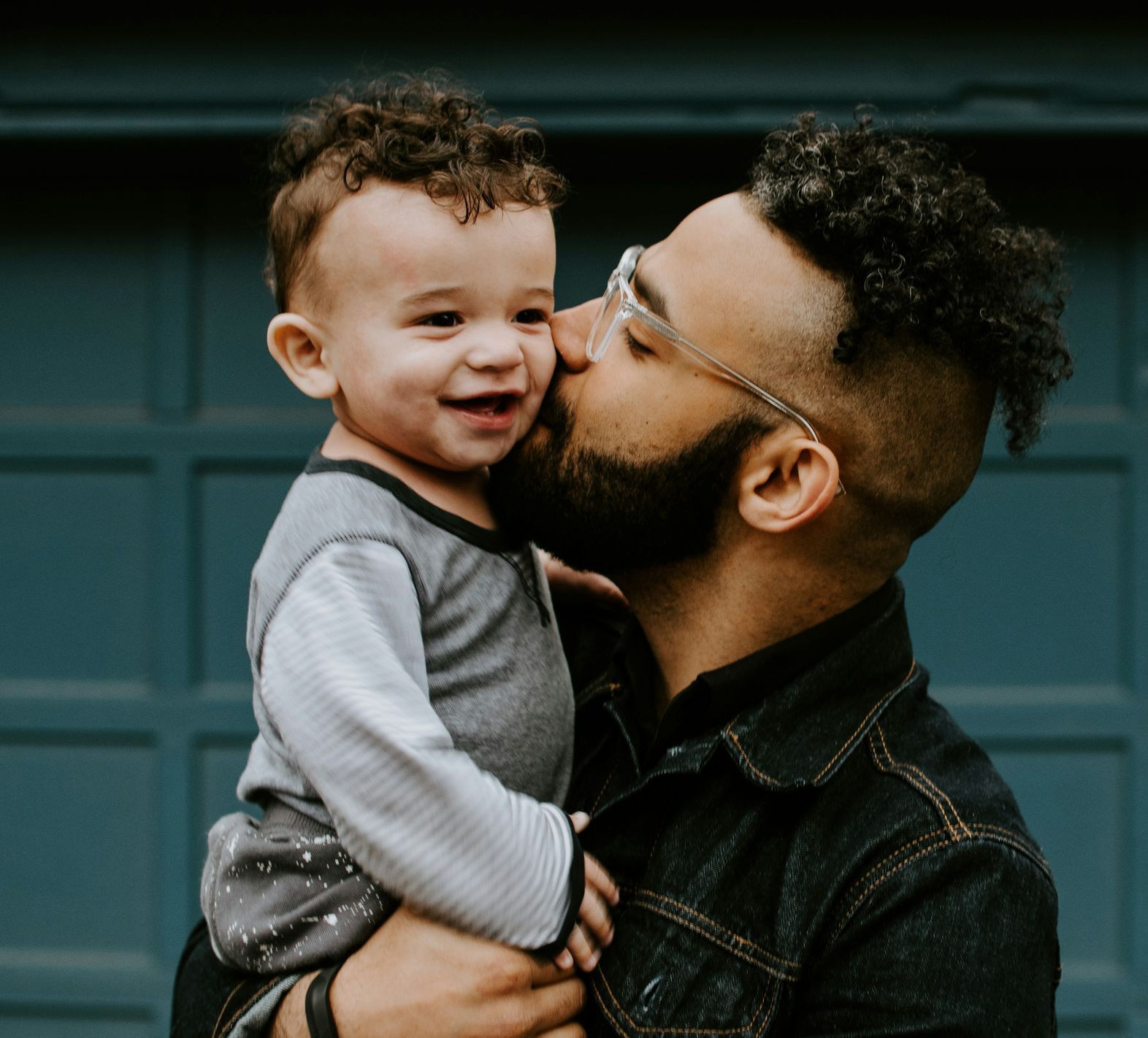 A man is holding a baby in his arms and kissing it on the cheek.