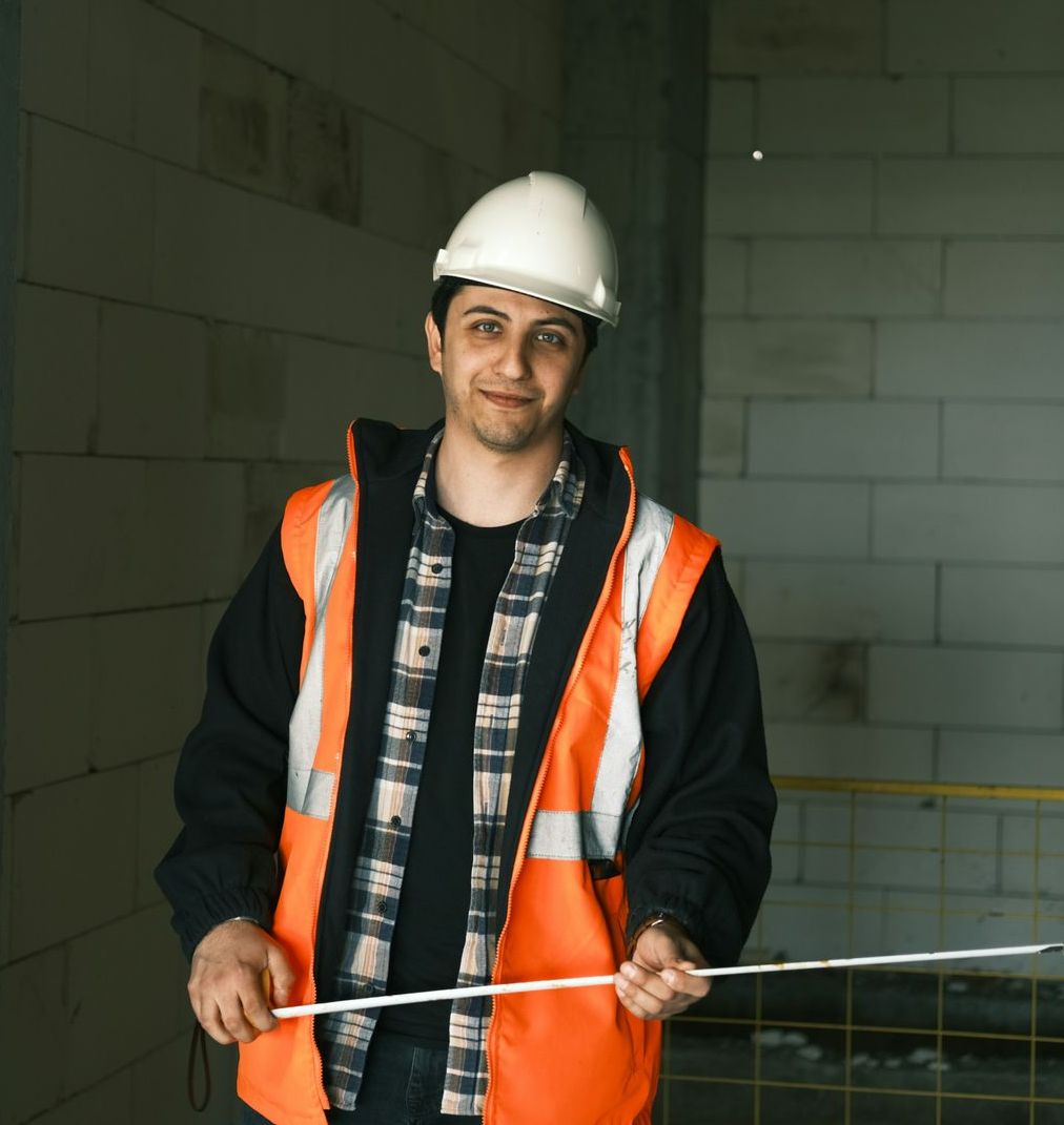 A man wearing a hard hat and an orange vest measures something