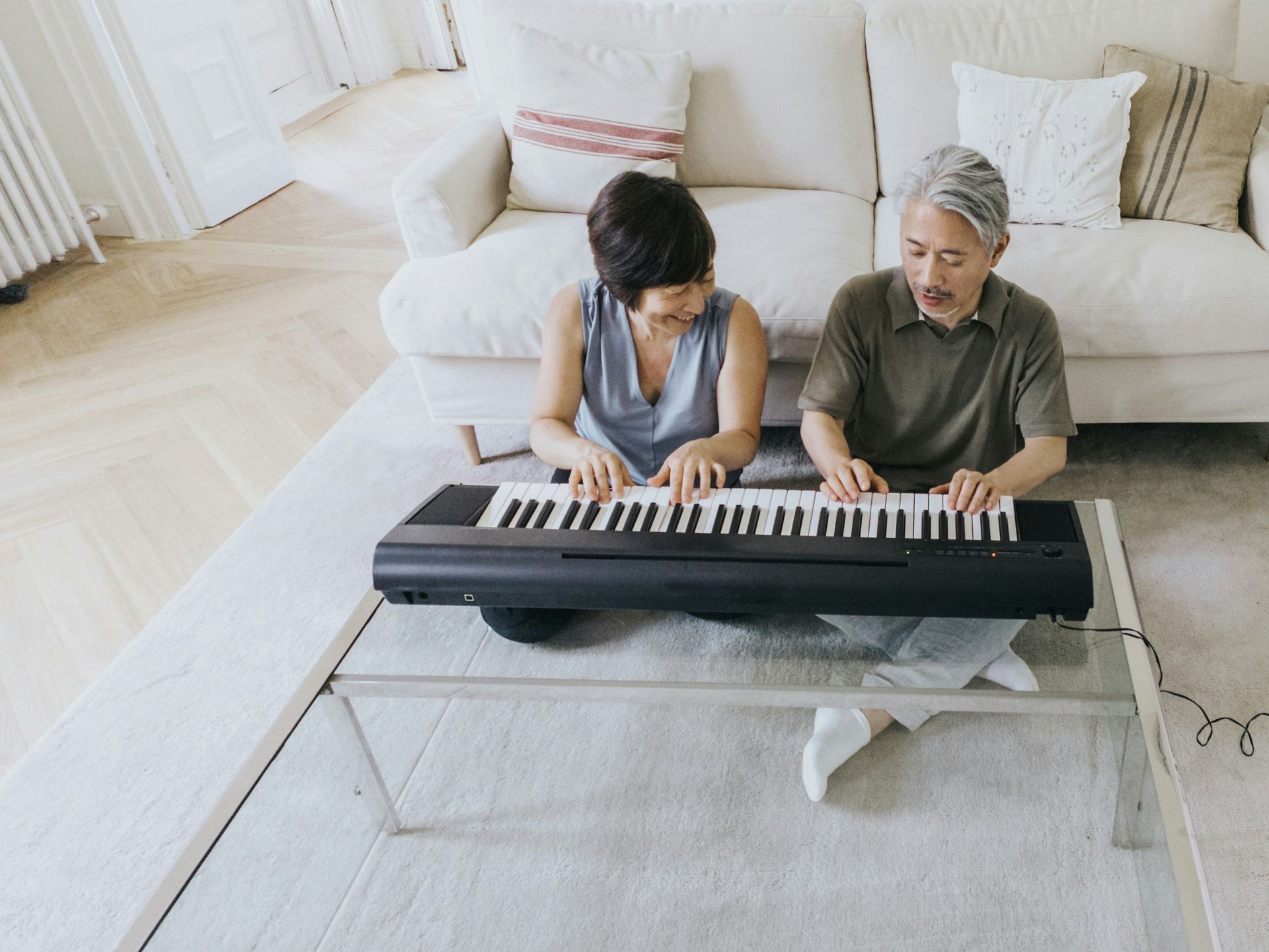 A man and a woman are sitting on the floor playing a keyboard.