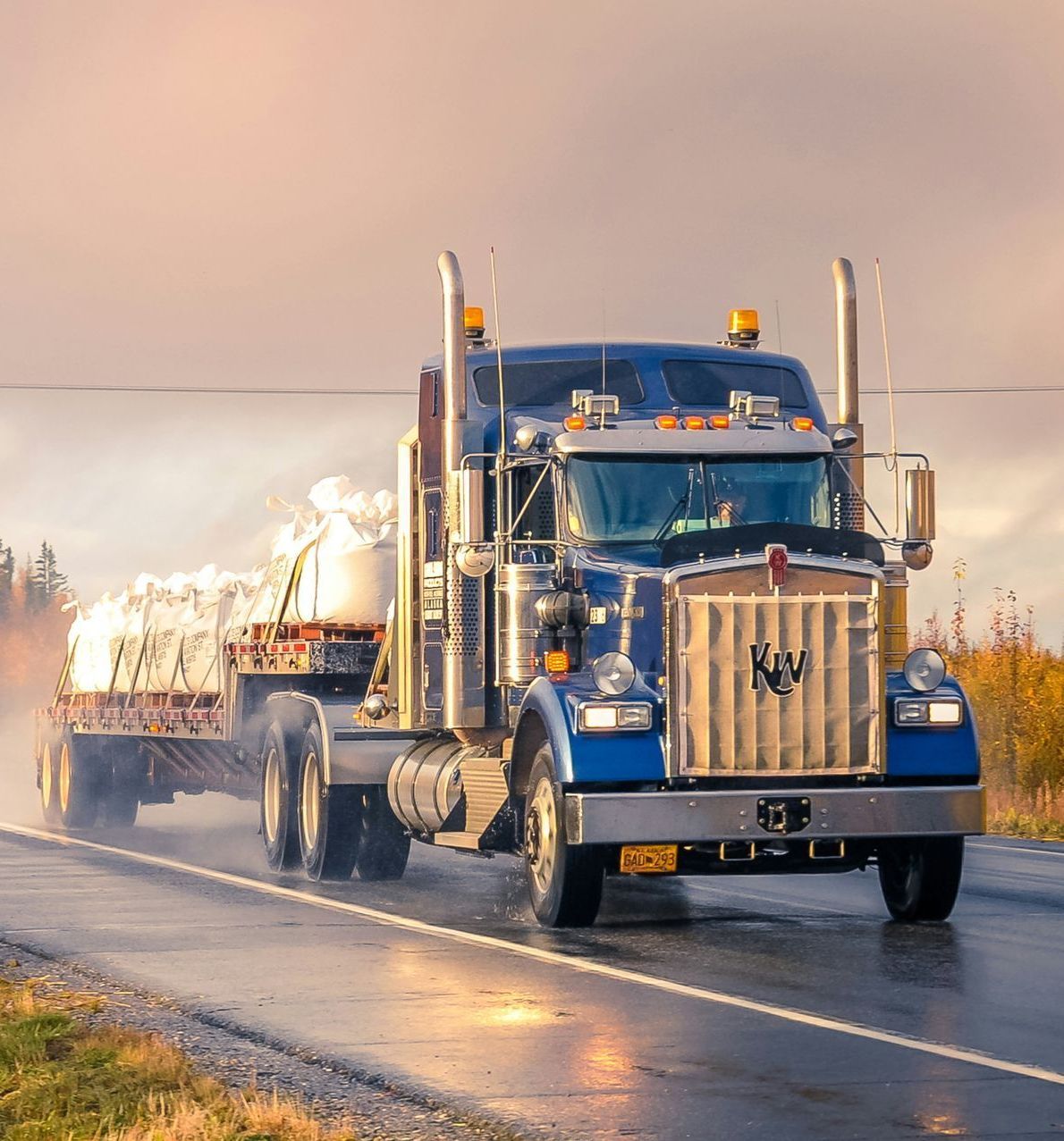 A blue semi truck is driving down a wet road.