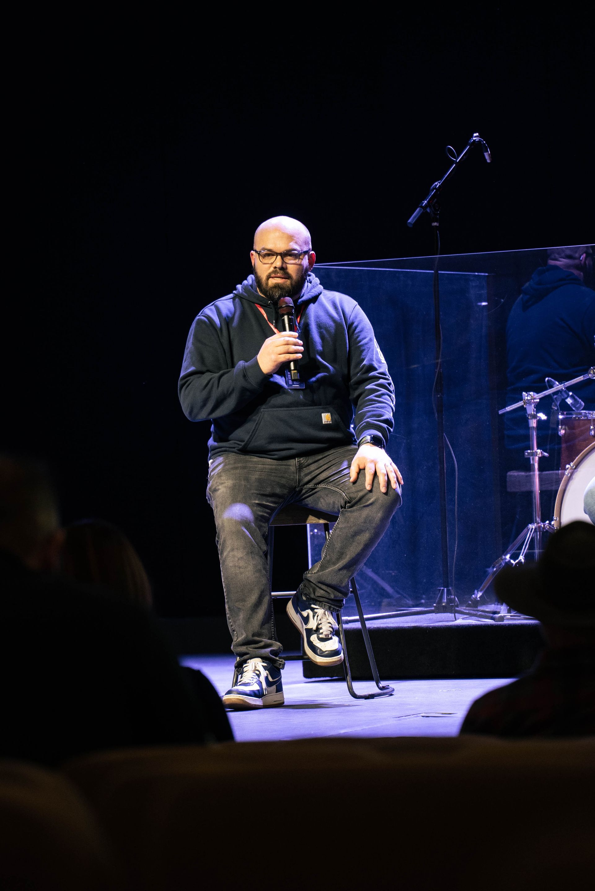 A man is sitting on a chair on a stage holding a microphone.