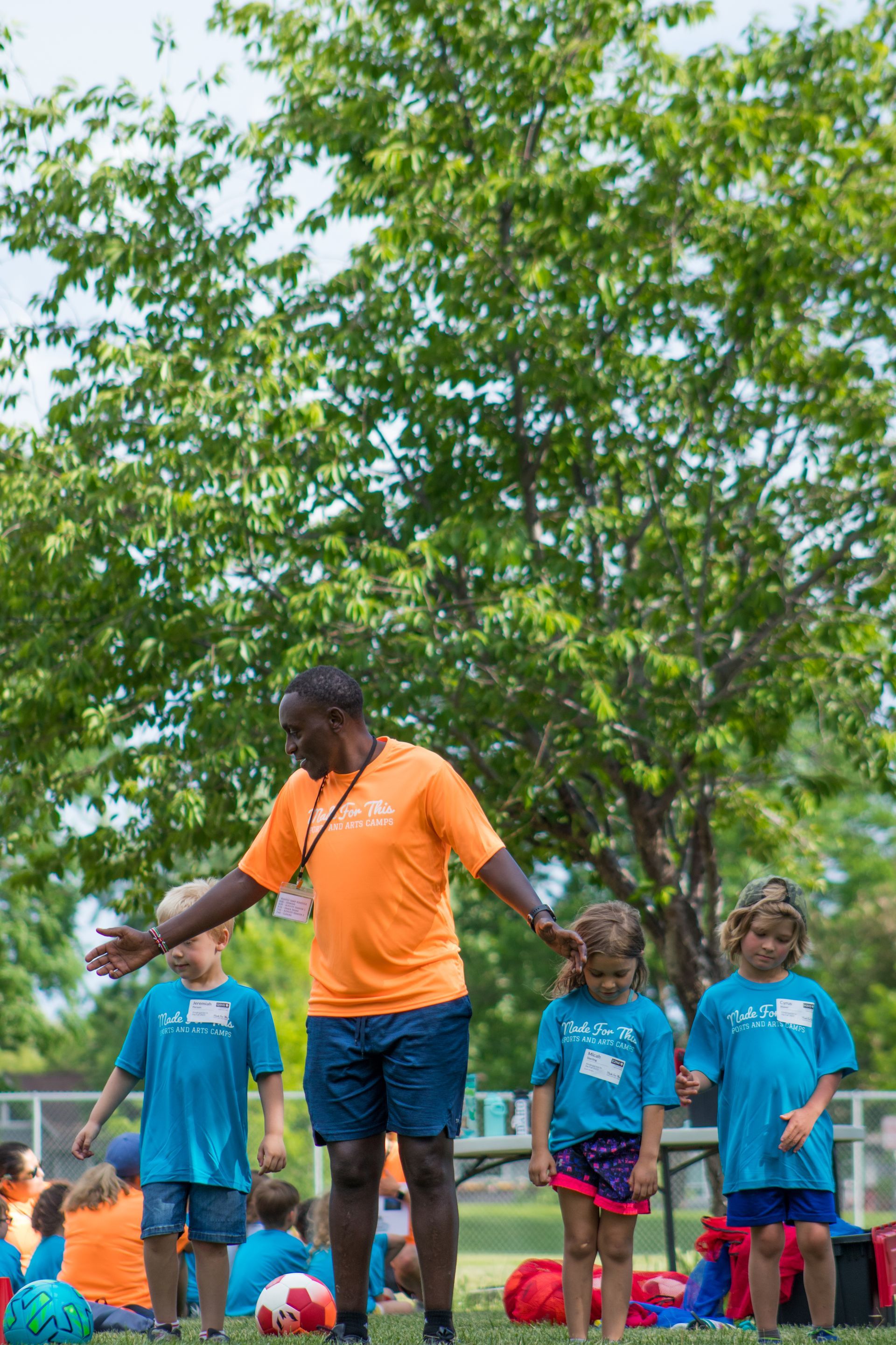 A man in an orange shirt is standing in front of a group of children.