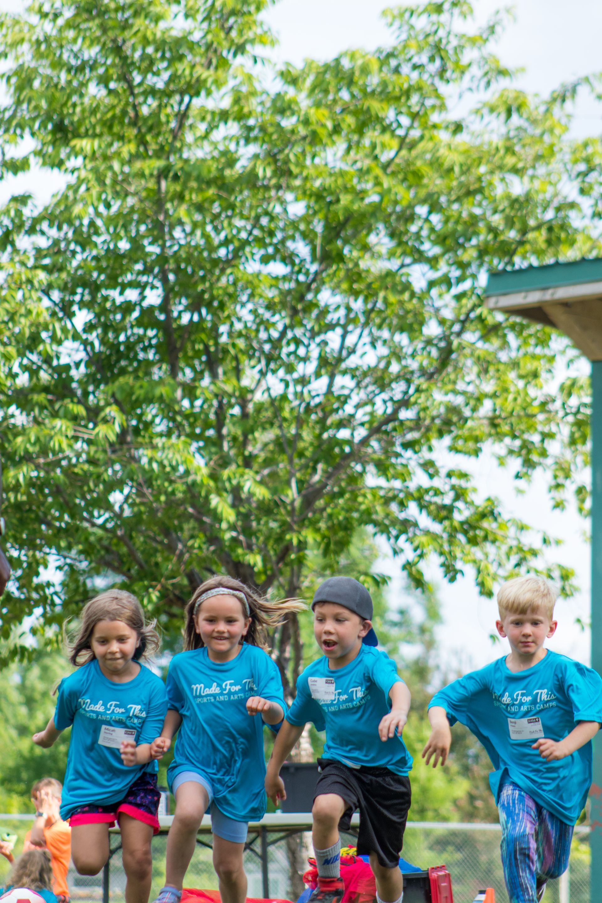 A group of children in blue shirts are running in a park.
