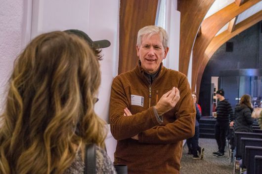 A man in a brown jacket is talking to a woman in a church.