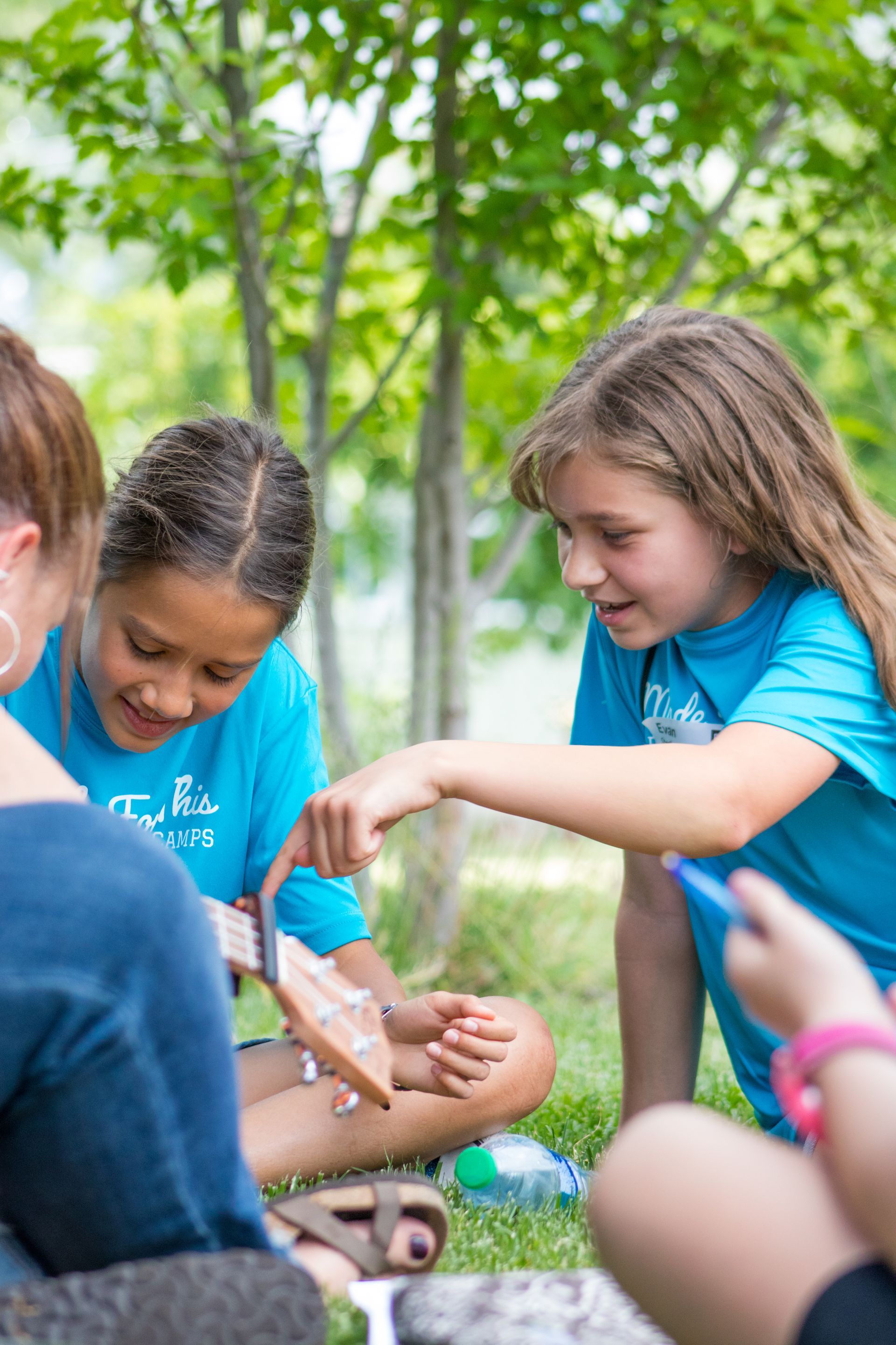 A group of young girls are sitting on the grass looking at a piece of wood.