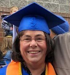 A woman wearing a blue graduation cap and gown is smiling.