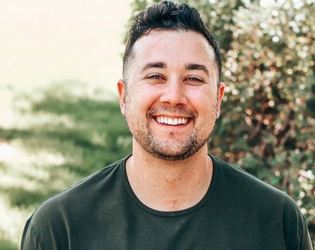 A man with a beard is smiling for the camera while wearing a green shirt.