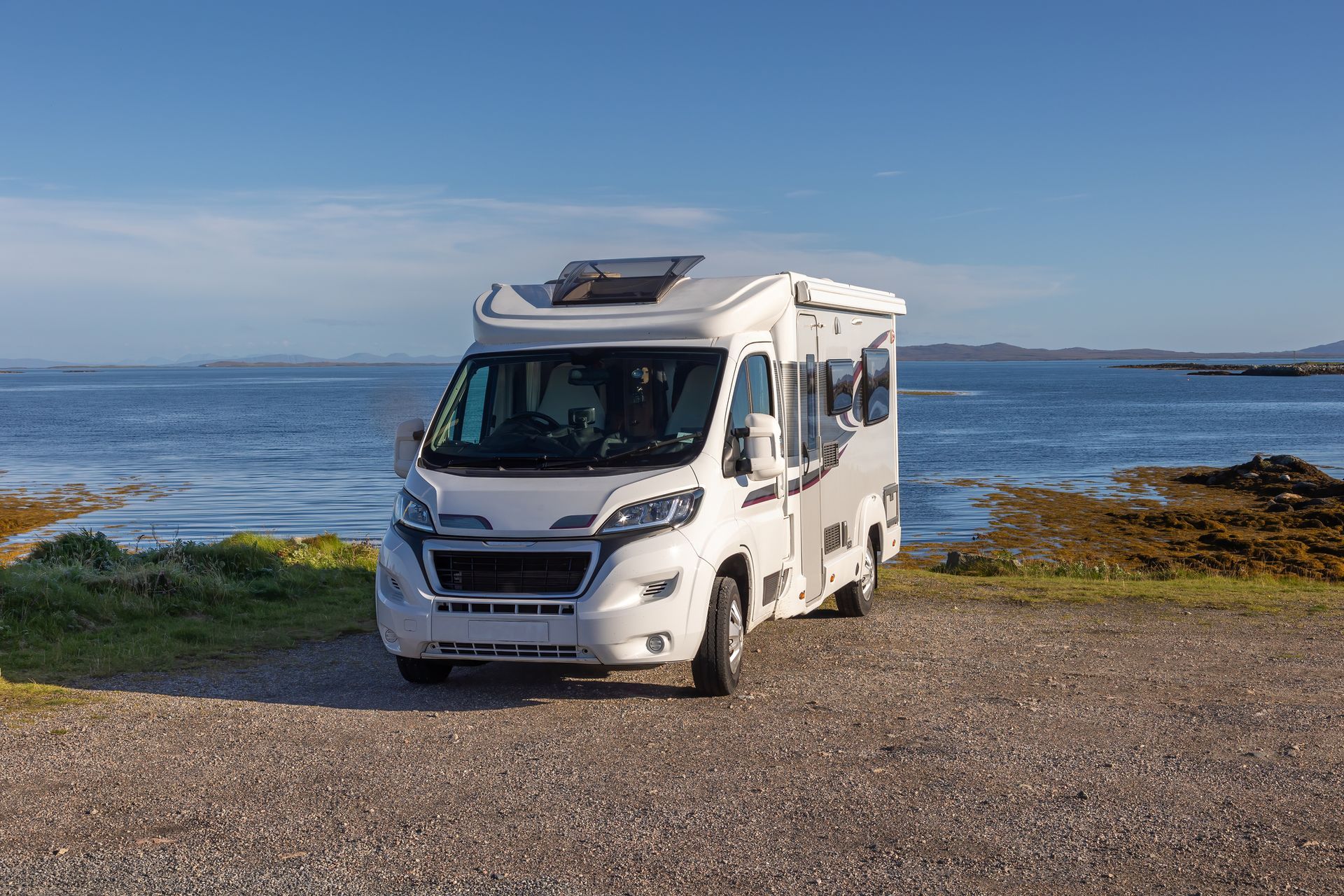 White campervan parked near a calm blue sea under a sunny sky.