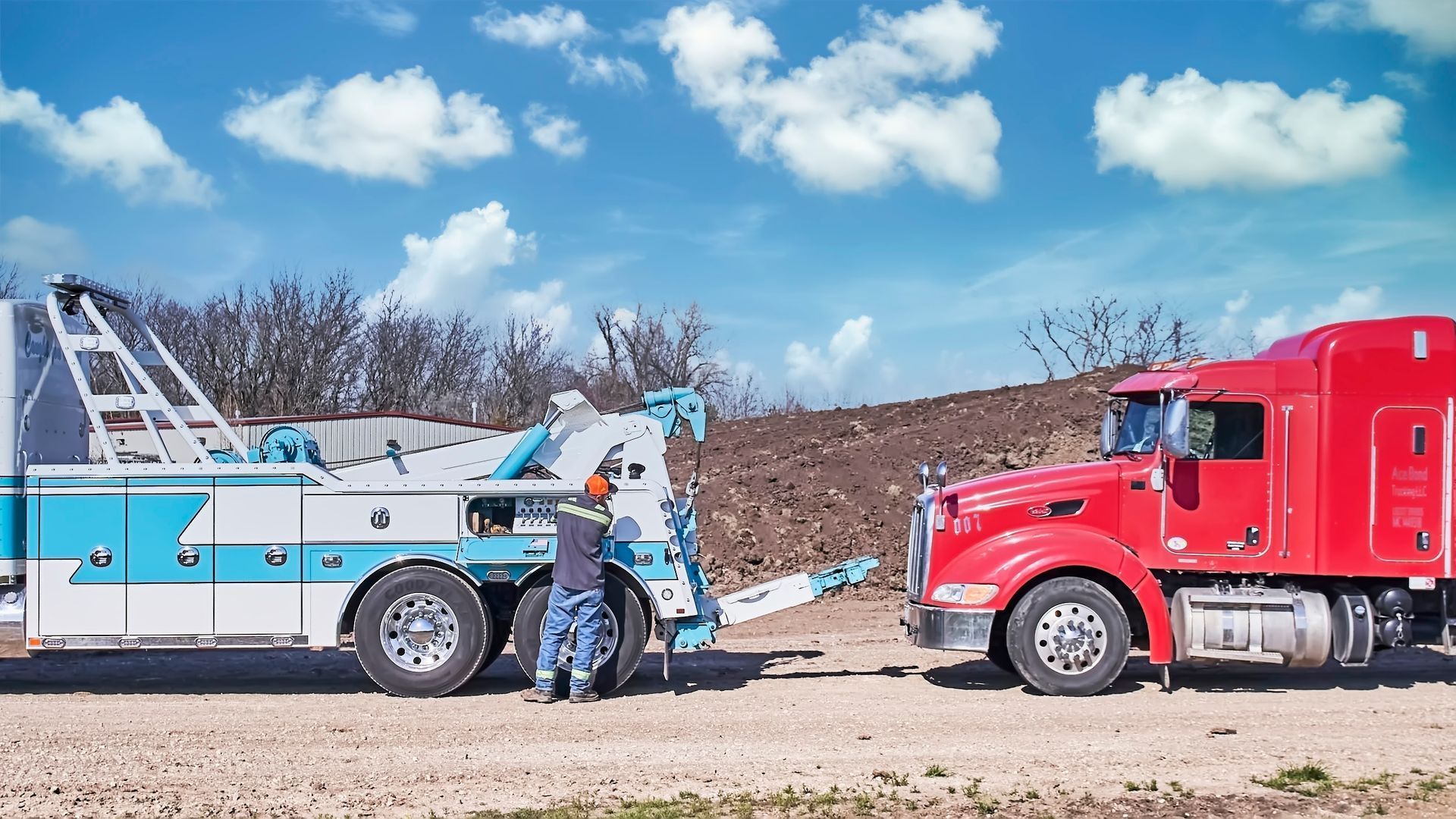 Tow truck operator hooks up a red semi-truck on a roadside under a blue sky