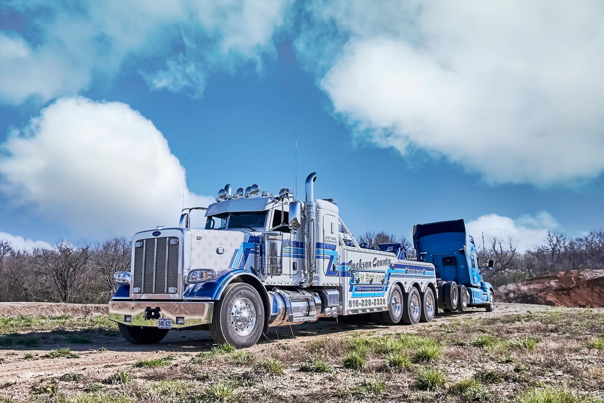 Blue semi truck with trailer on a rural dirt field under a cloudy sky