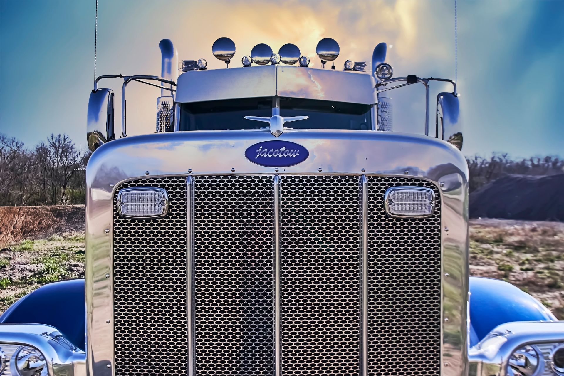 Front view of a blue classic semi truck with chrome grille and lights, parked outdoors under a clear sky