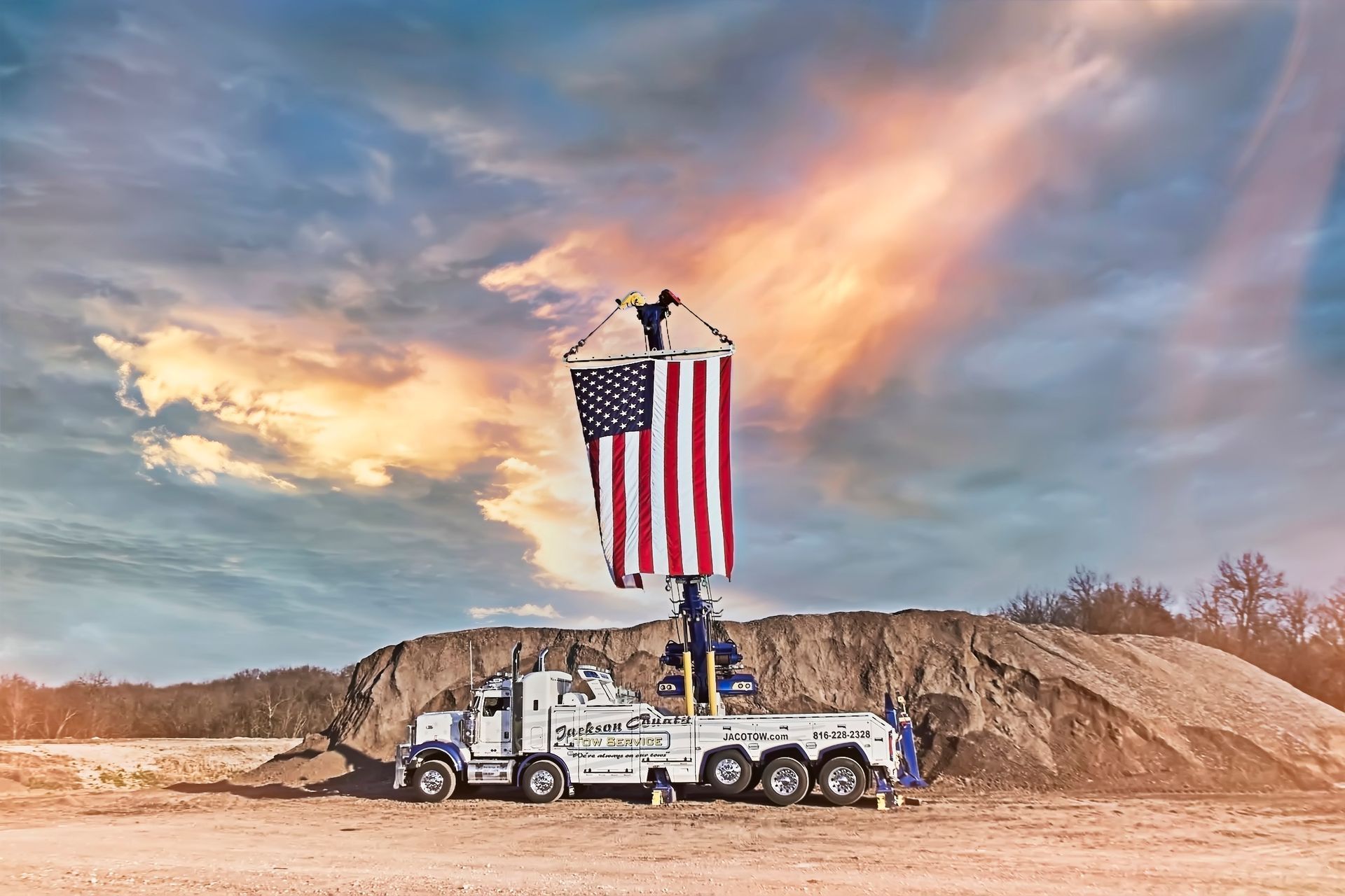 Two workers hoist a large American flag above a truck at a construction site at sunset