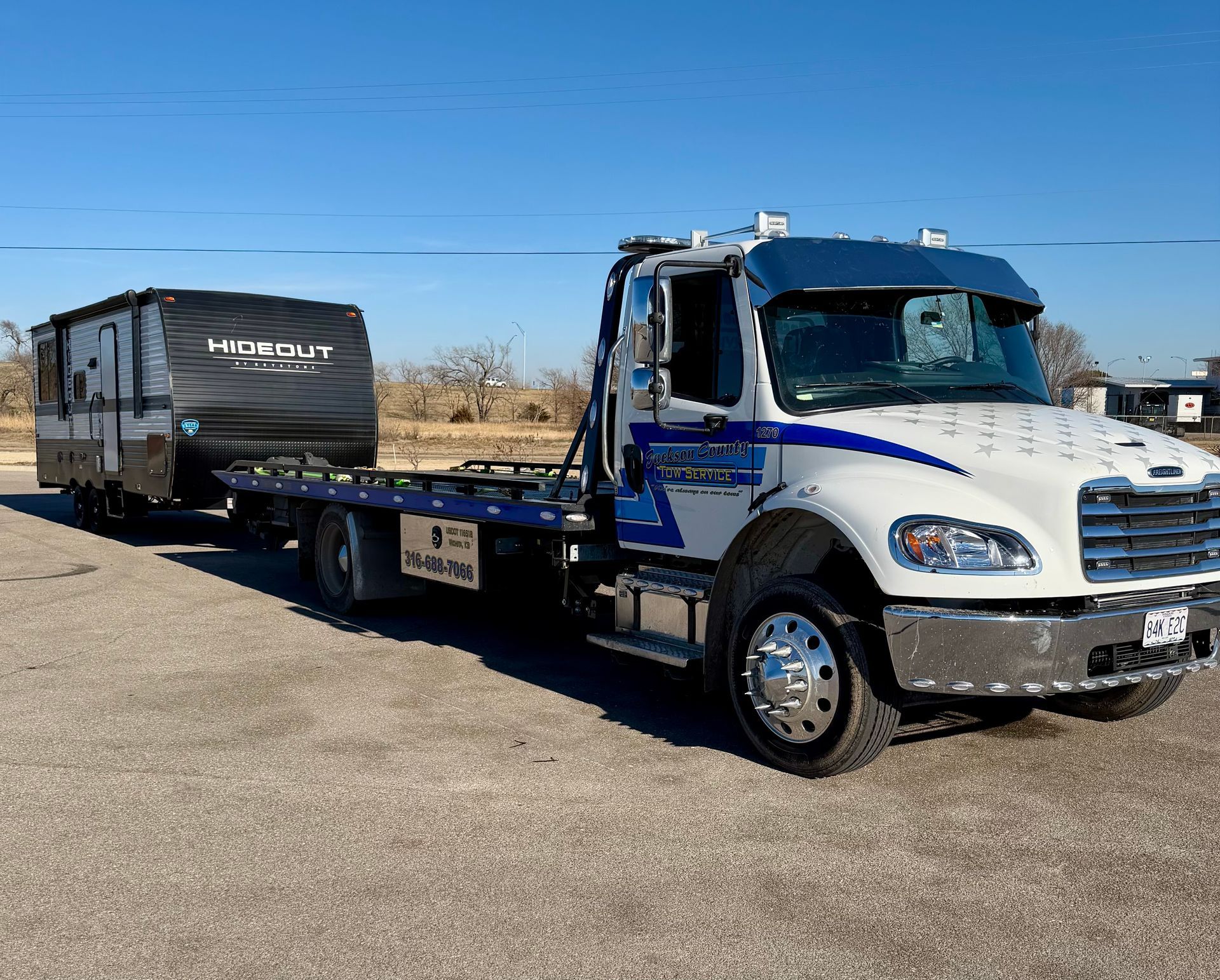 White flatbed tow truck parked on pavement under a clear blue sky