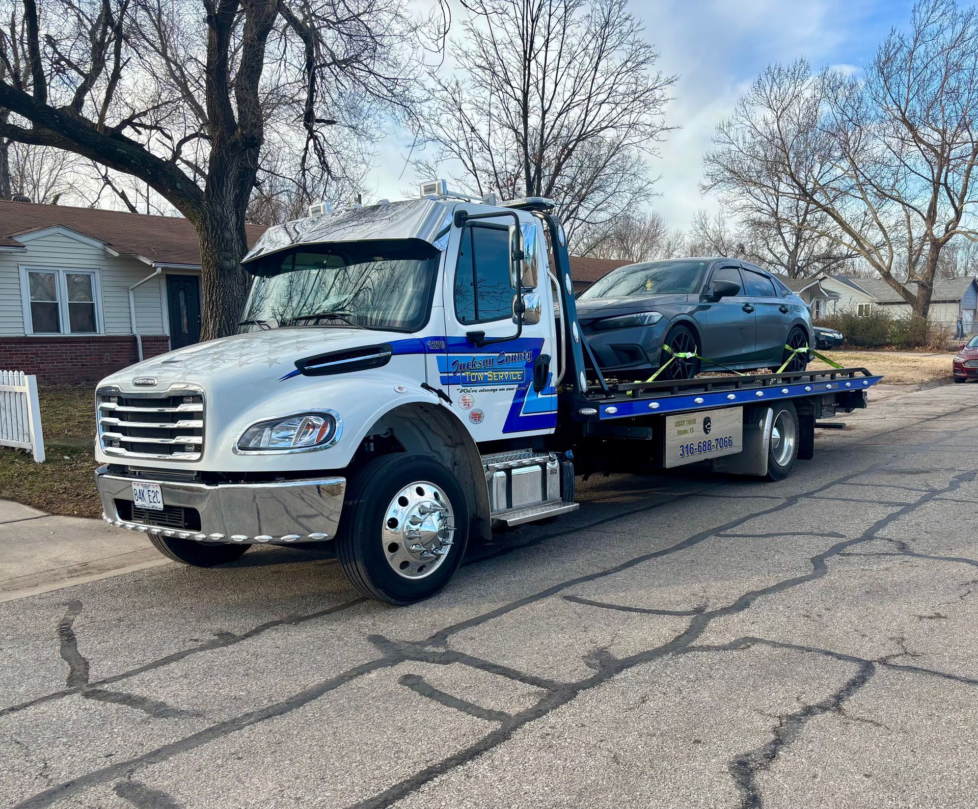 Blue flatbed tow truck carrying a black SUV on a cracked residential street