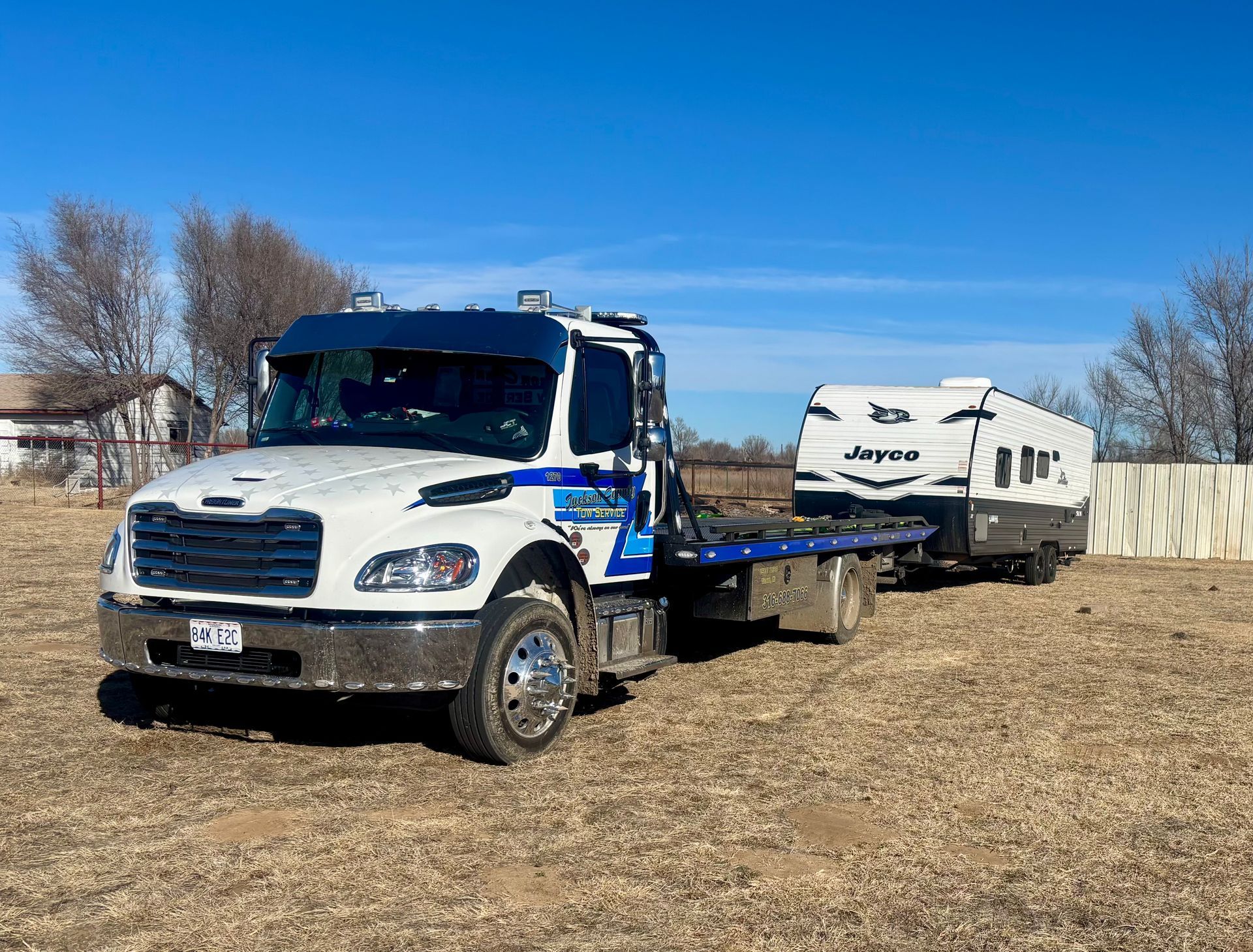 White and blue tow truck hauling a white RV across a dry field under a clear blue sky