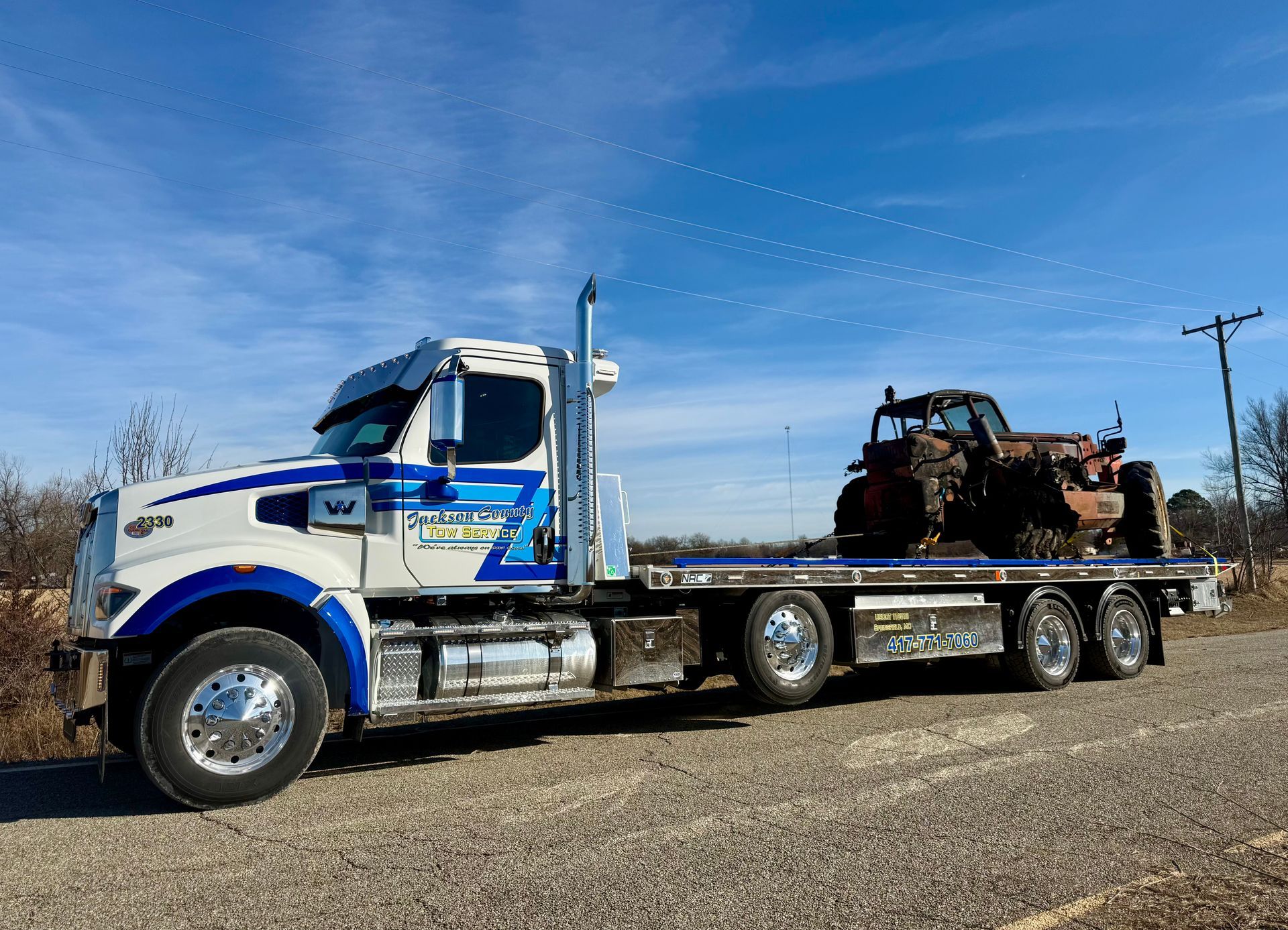 White semi-truck hauling a rusted vehicle on a flatbed trailer under a clear blue sky
