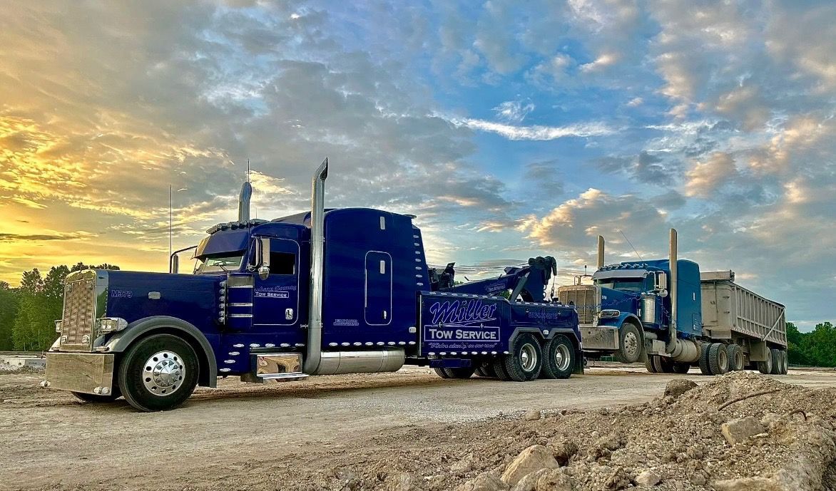 Blue semi-truck hauling a trailer on a dirt road at sunset under a cloudy sky