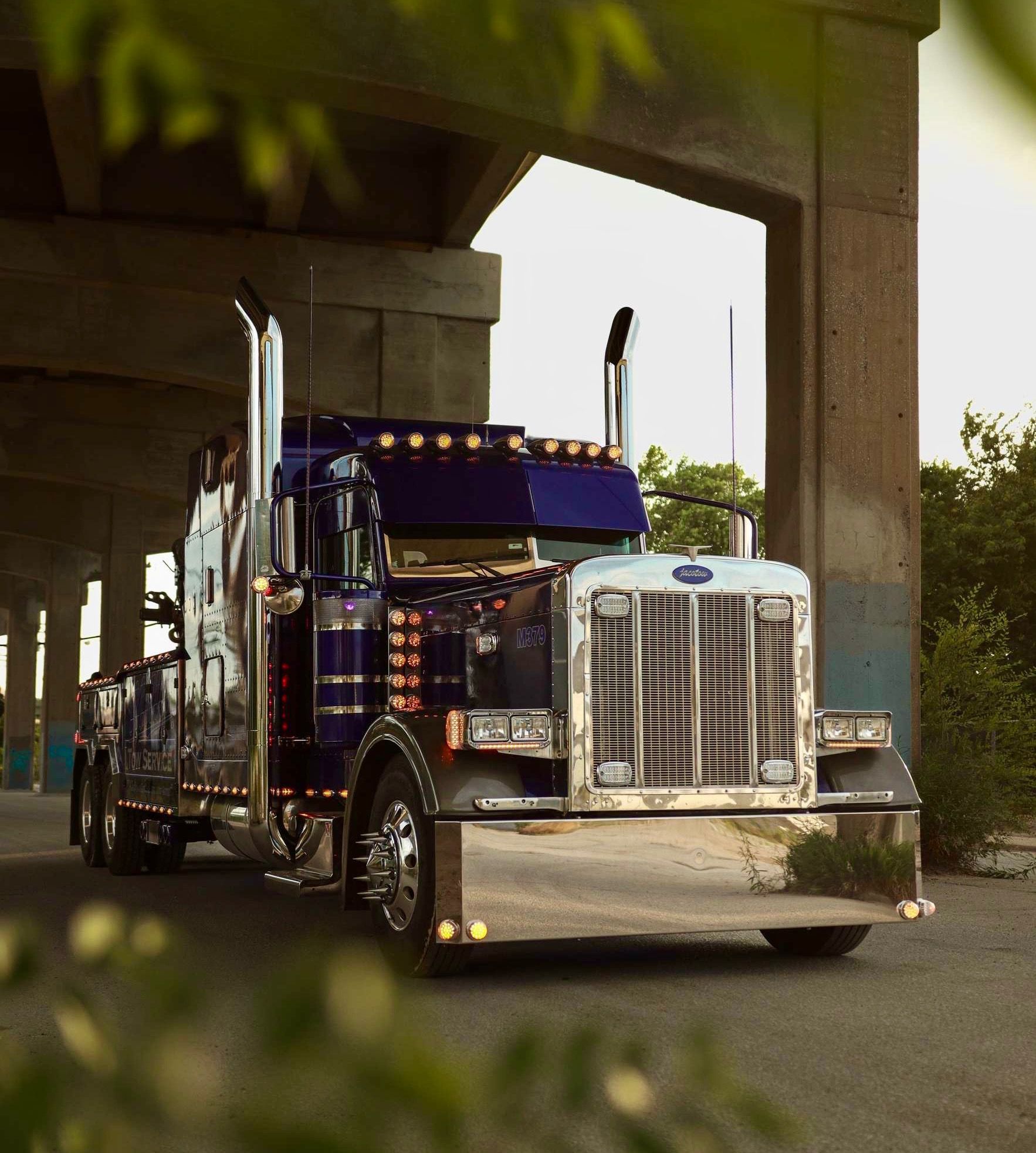 Large black semi-truck with chrome grille parked under an overpass