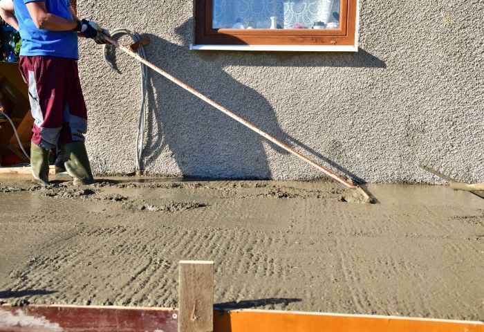 Worker smoothing a freshly poured concrete slab with a bull float