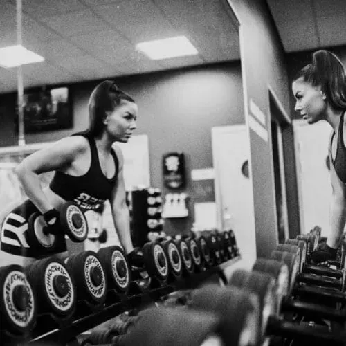 A person performing a single-arm dumbbell row in a gym, reflected in a mirror.