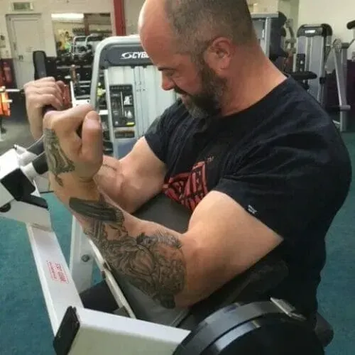 A muscular person with tattoos on their arm performs a bicep curl exercise on a gym machine.