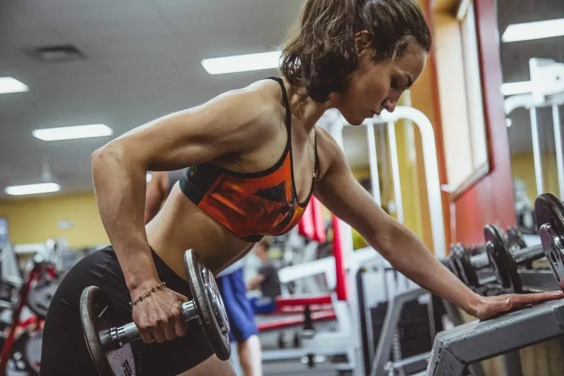 A person in an orange athletic top performing a single-arm dumbbell row at a gym.