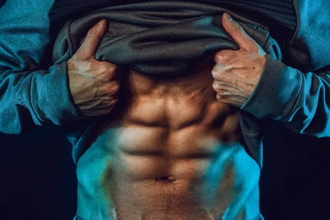 A person lifting their shirt to reveal well-defined abdominal muscles under dramatic blue lighting.