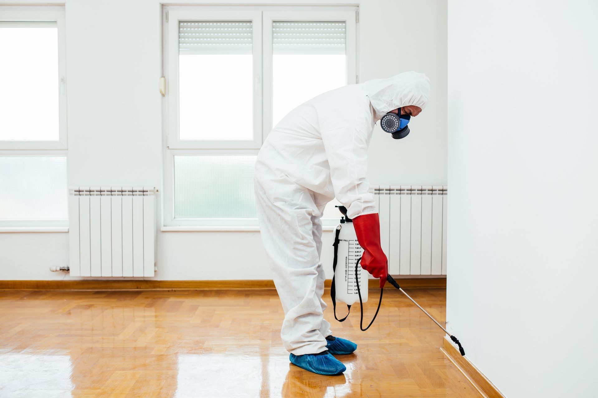 Worker sanding a wooden floor with a power sander in a bright empty room