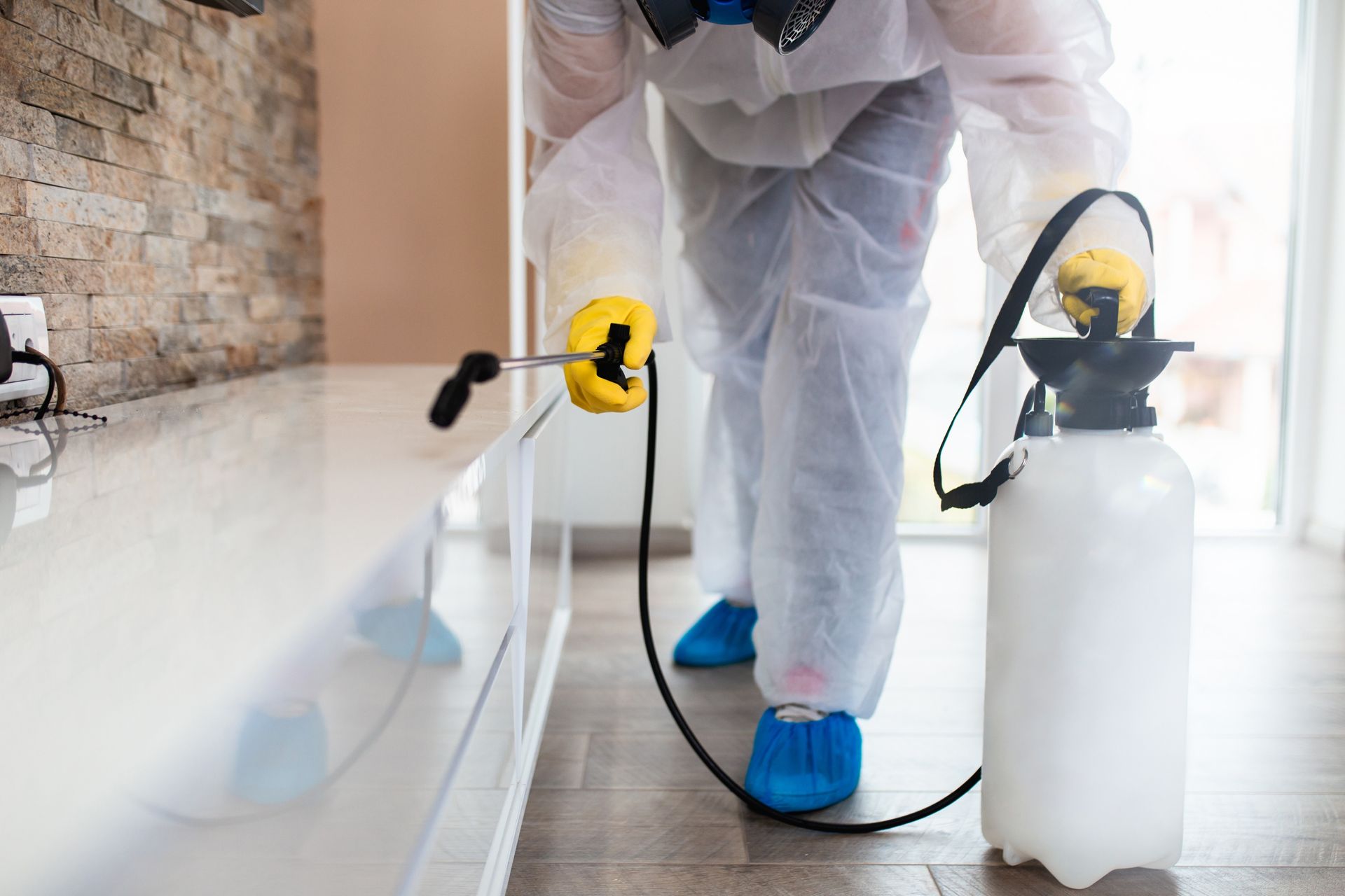 Technician in protective gear spraying disinfectant along a bathroom or kitchen floor with a cleaning machine