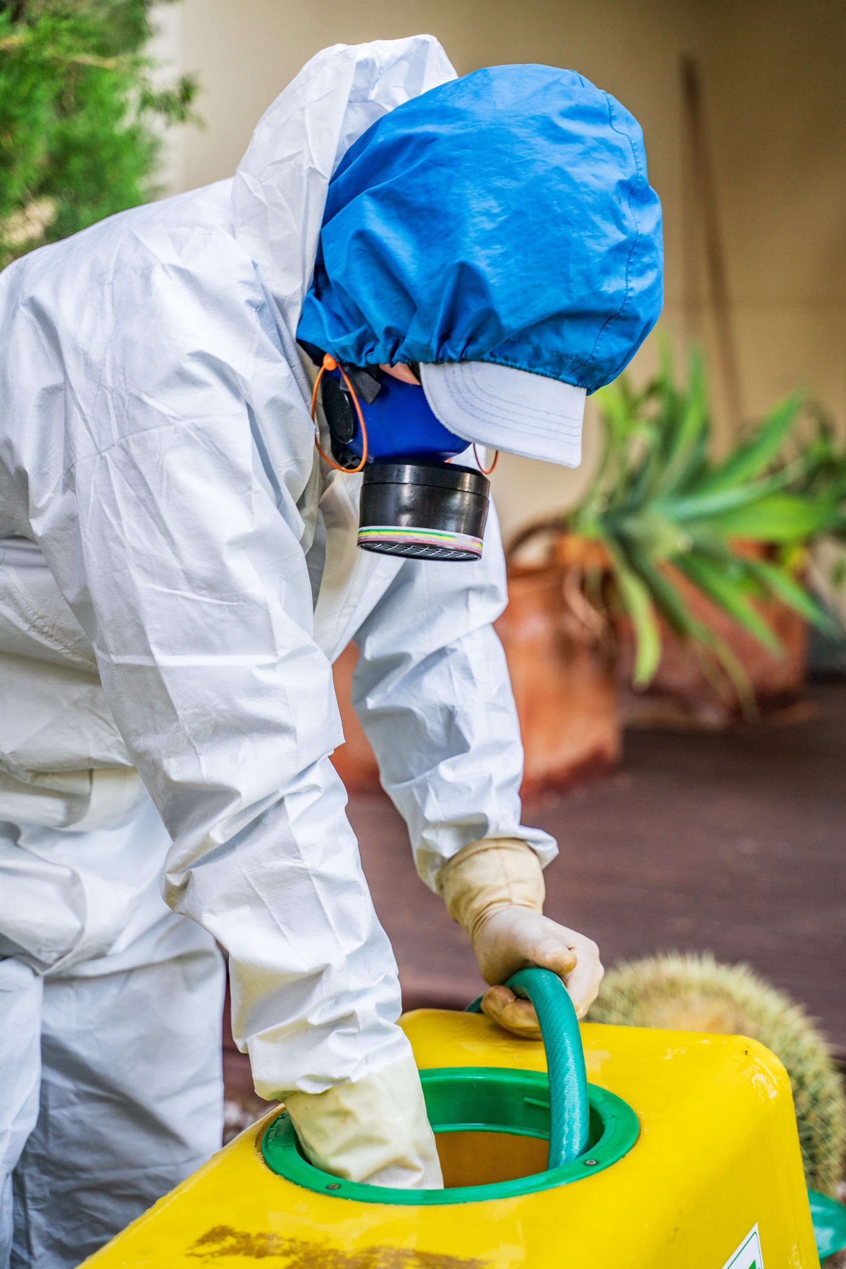 Person in protective suit disinfecting a yellow container with a green hose outdoors