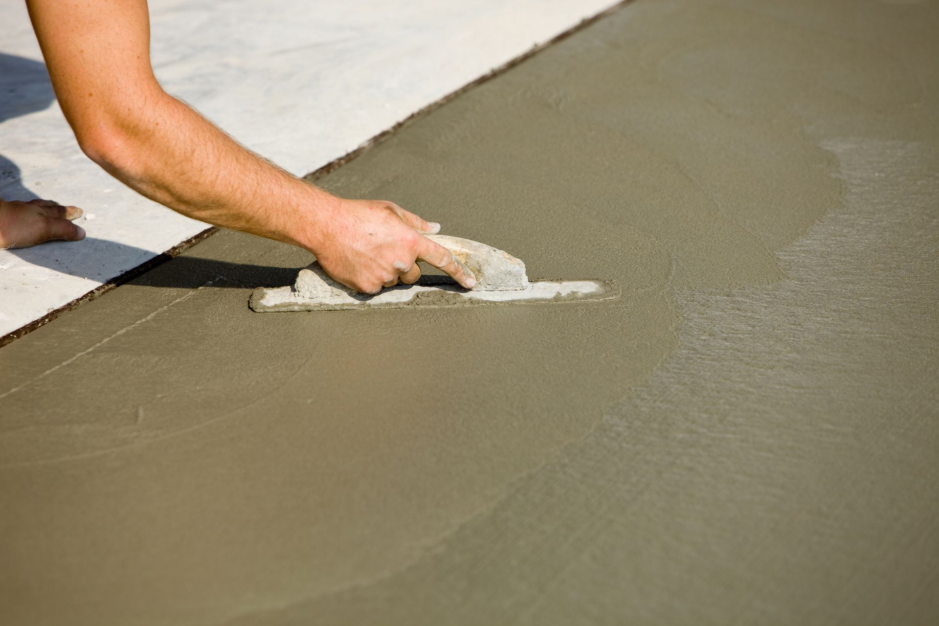 A man is spreading concrete on a sidewalk with a trowel.